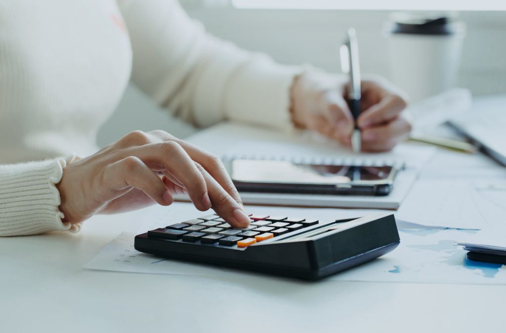 A person using a calculator and writing in a notebook, calculating financial changes related to Employers Allowance 2025.